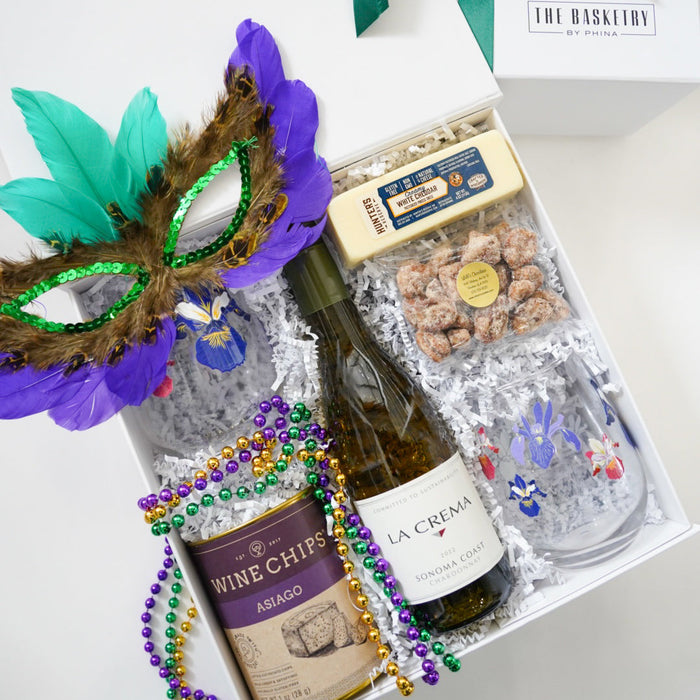 Gift basket with wine, snacks, and Mardi Gras mask on a white background