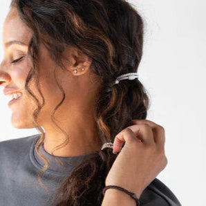 Smiling woman tying her curly hair into a ponytail, with hair ties on her wrist