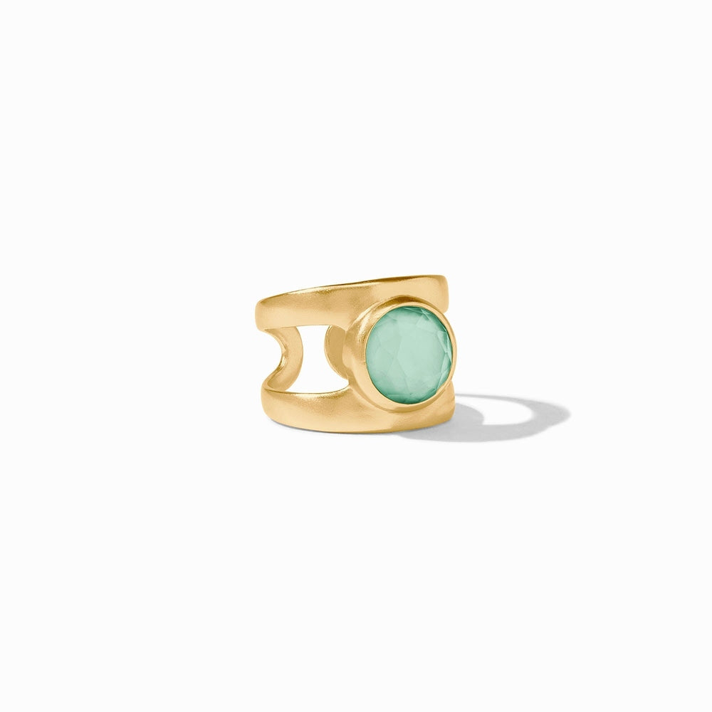 Gold-plated jewelry by Julie Vos featuring a round faceted aqua green gemstone and a wide brushed band with circular side cutouts on a minimalist white background