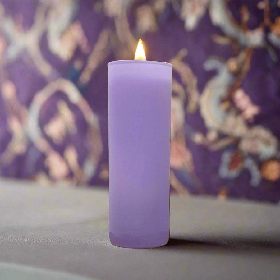 Lit lavender votive candle in front of purple patterned fabric