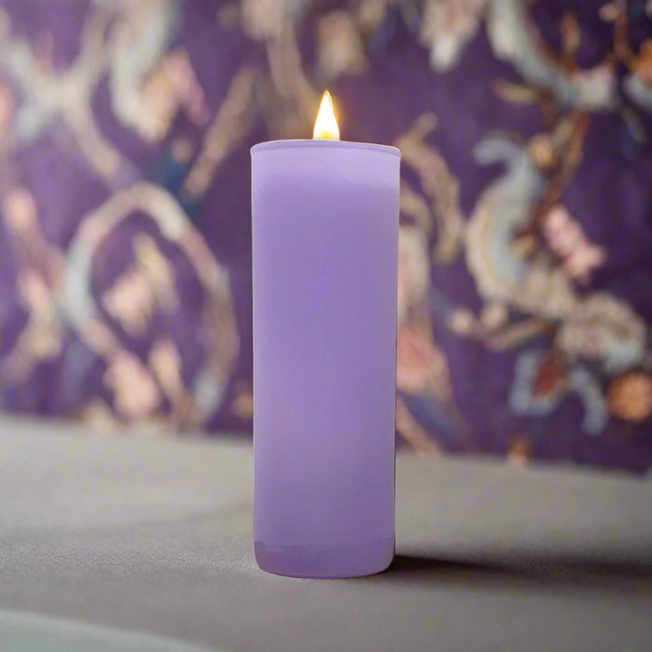 Lit lavender votive candle in front of purple patterned fabric