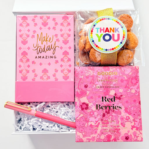 Gift set with pink notebook, pen, and cookies in a box on a white background