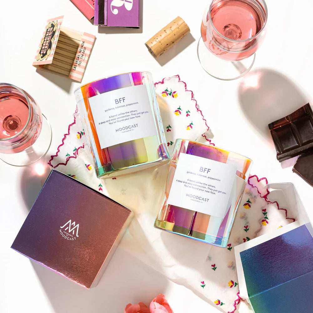 Photograph by Moodcast Fragrance Co of iridescent glass BFF candles in a flat-lay arrangement featuring pink wine, a vintage Circus Circus Las Vegas matchbook, and squares of dark chocolate