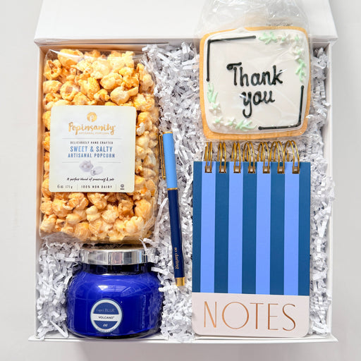 Gift set with popcorn, candle, and stationery items in a clear bag on a white background