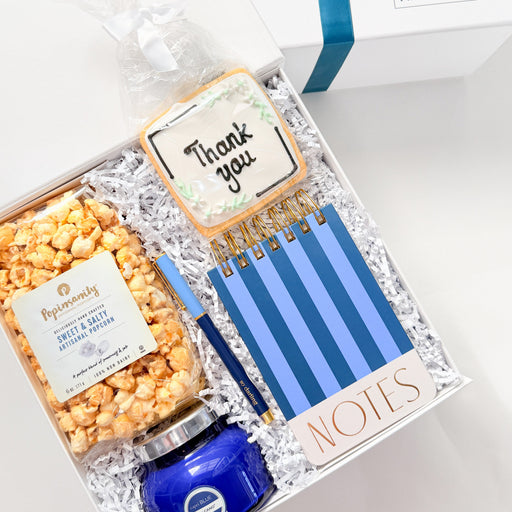 Gift set with popcorn, blue pen, and striped notepad in a decorative box.