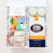 A curated gift box set containing a Mariah & Fitt Southern Pecan box, a bag of French Market ground coffee, two cream macarons, a ceramic mug, and a small gold ring, all arranged in white crinkle paper inside an open white gift box.