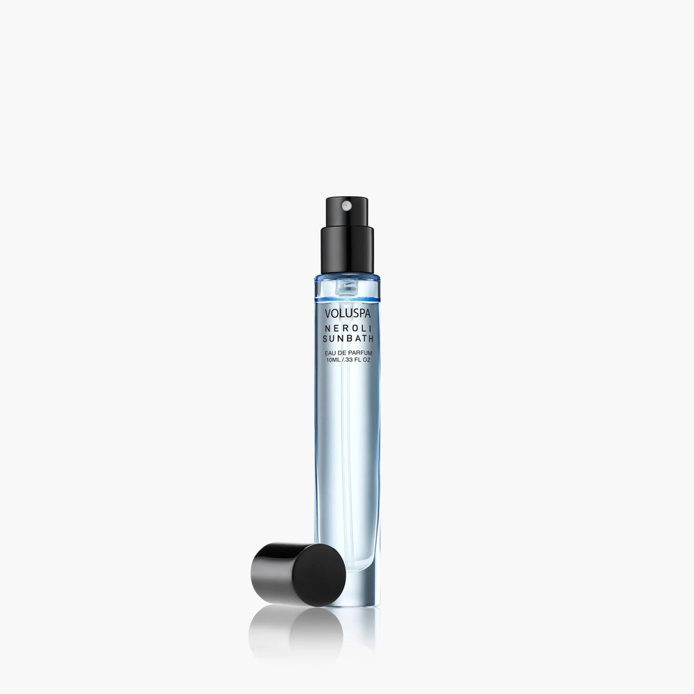 Studio photography by Voluspa of a Neroli Sunbath travel spray bottle featuring light blue liquid, minimalist black typography, and a detached black cap on a white reflective surface