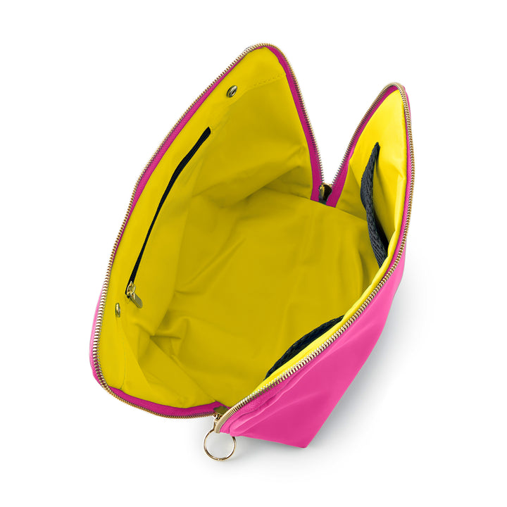 Studio photograph of a vibrant pink nylon cosmetic bag opened wide on a white background featuring a bright yellow interior lining gold-toned zipper with a circular ring pull and internal black mesh organizational pockets