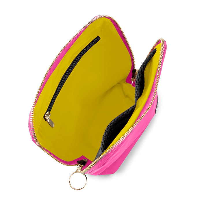 Studio product photograph of an open neon pink accessory bag against a white background featuring a vibrant yellow interior lining, a black mesh pocket, and gold-tone zippers with a large circular pull ring