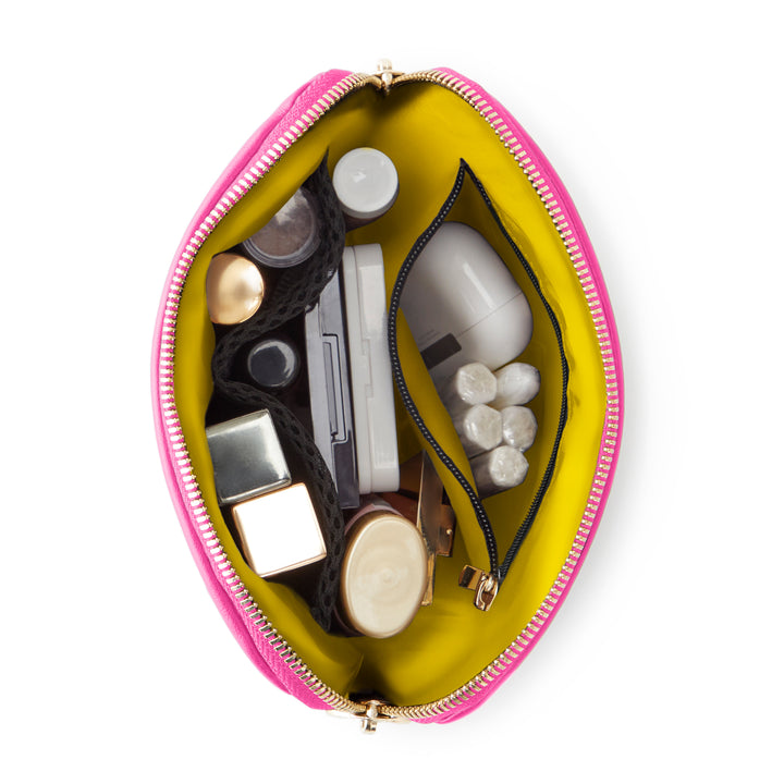 Digital photograph of an open pink cosmetic bag on a white background featuring a vibrant lime yellow lining, gold hardware, and beauty essentials organized within a black mesh pocket