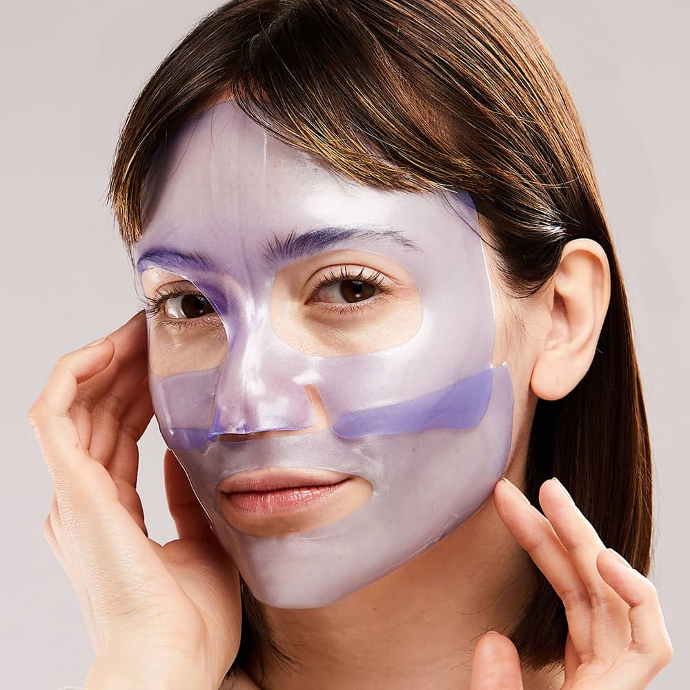 Digital photograph of a woman wearing a translucent lavender hydrogel face mask in a studio setting with a shimmering purple finish and precise cutouts for her brown eyes and lips