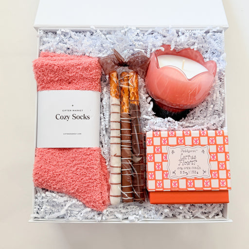 Gift set with coral socks, candle, and other items in a box on a white background