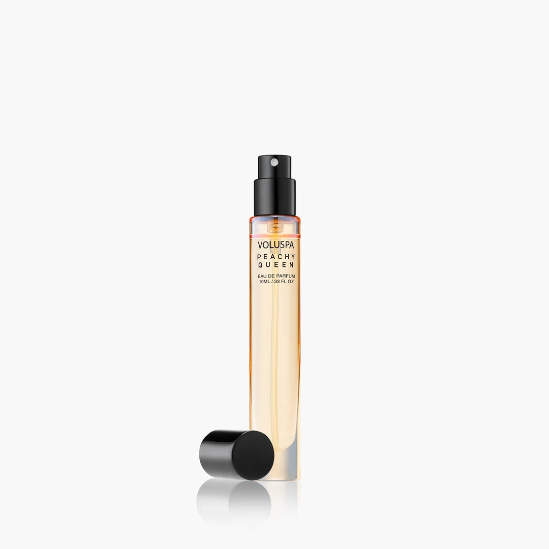 Product photograph of Voluspa Peachy Queen Eau de Parfum featuring a 10ml slim glass travel spray bottle with peach-toned liquid, a black atomizing nozzle, and a detached black cap on a white reflective surface