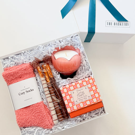 Gift set with pink socks, candles, and other items in a decorative box on a white background