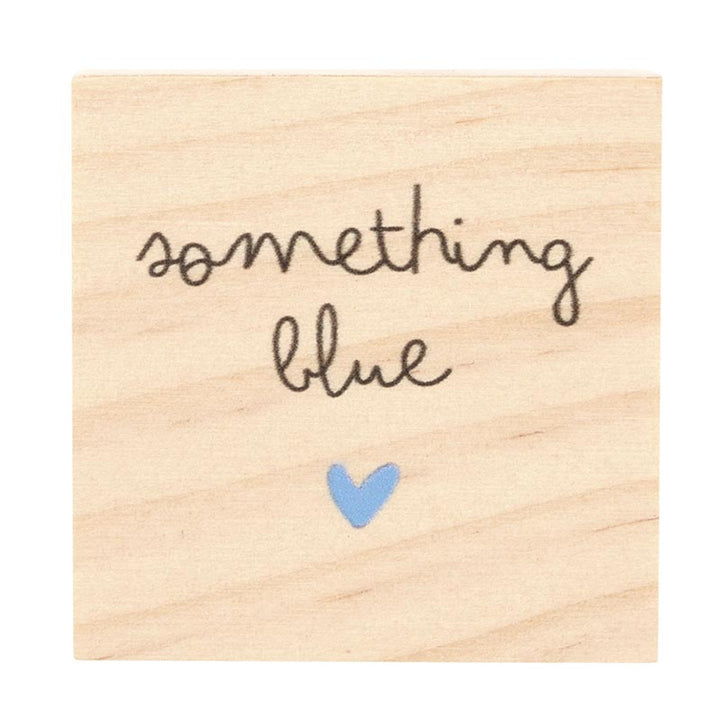 Wooden rubber stamp featuring the hand-lettered cursive phrase something blue and a small light blue heart centered on a natural wood grain background
