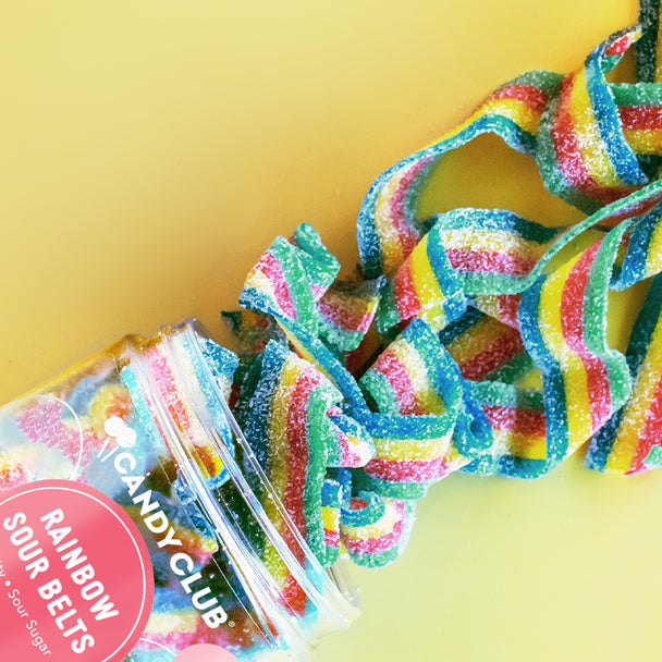 Rainbow sour belt candy spilling from a Candy Club jar on a yellow background