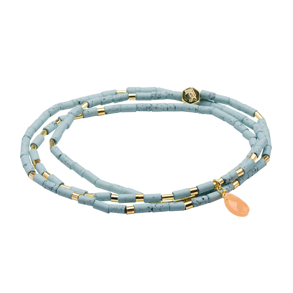 Beaded wrap bracelet by Kendra Scott featuring marbled dusty blue cylinder beads, gold-tone metal spacers, and a translucent peach teardrop gemstone charm on a white background alongside the iconic signature logo medallion