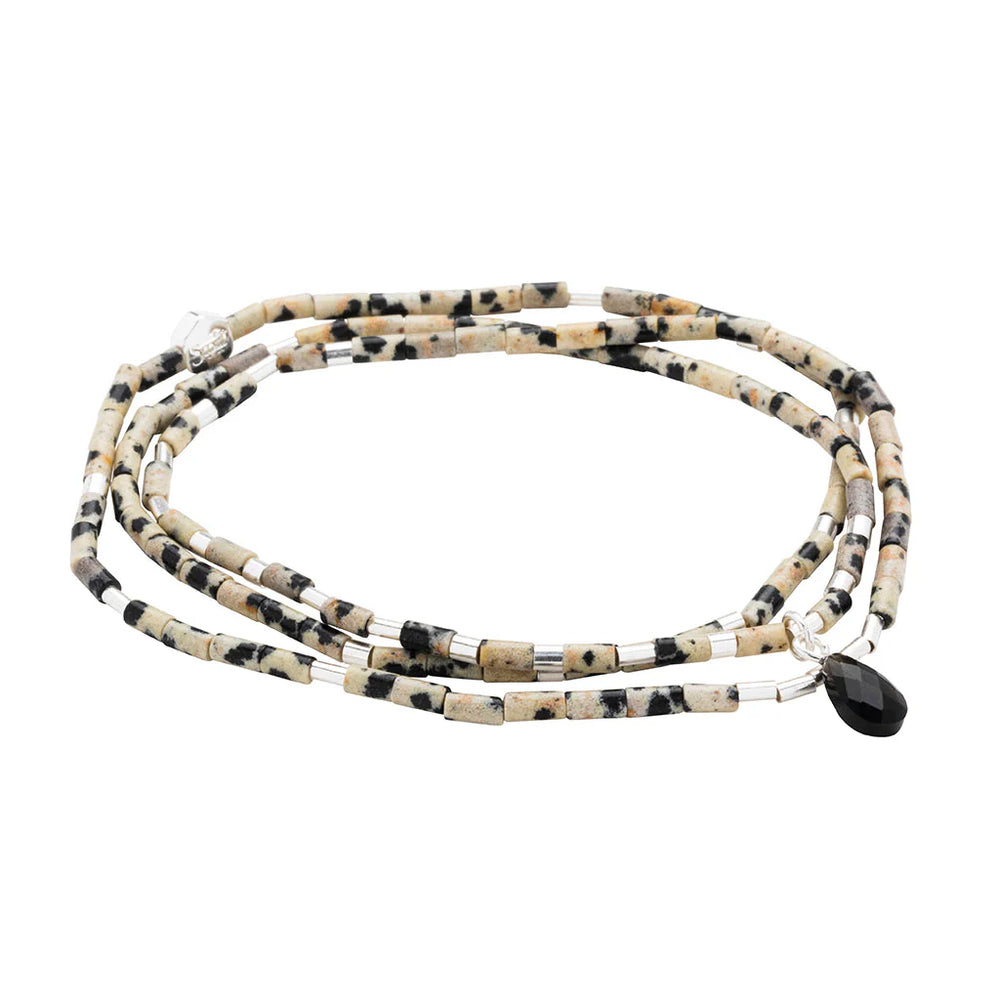 Handmade dalmatian jasper multi-wrap bracelet by Scout Curated Wear featuring cylindrical spotted beige beads, shimmering silver spacers, and a single faceted black teardrop charm on a white background