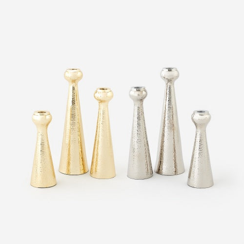 Hammered metal taper candle holders in gold and silver finishes displayed on a white background featuring a textured dimpled surface and varying heights in a modern conical silhouette