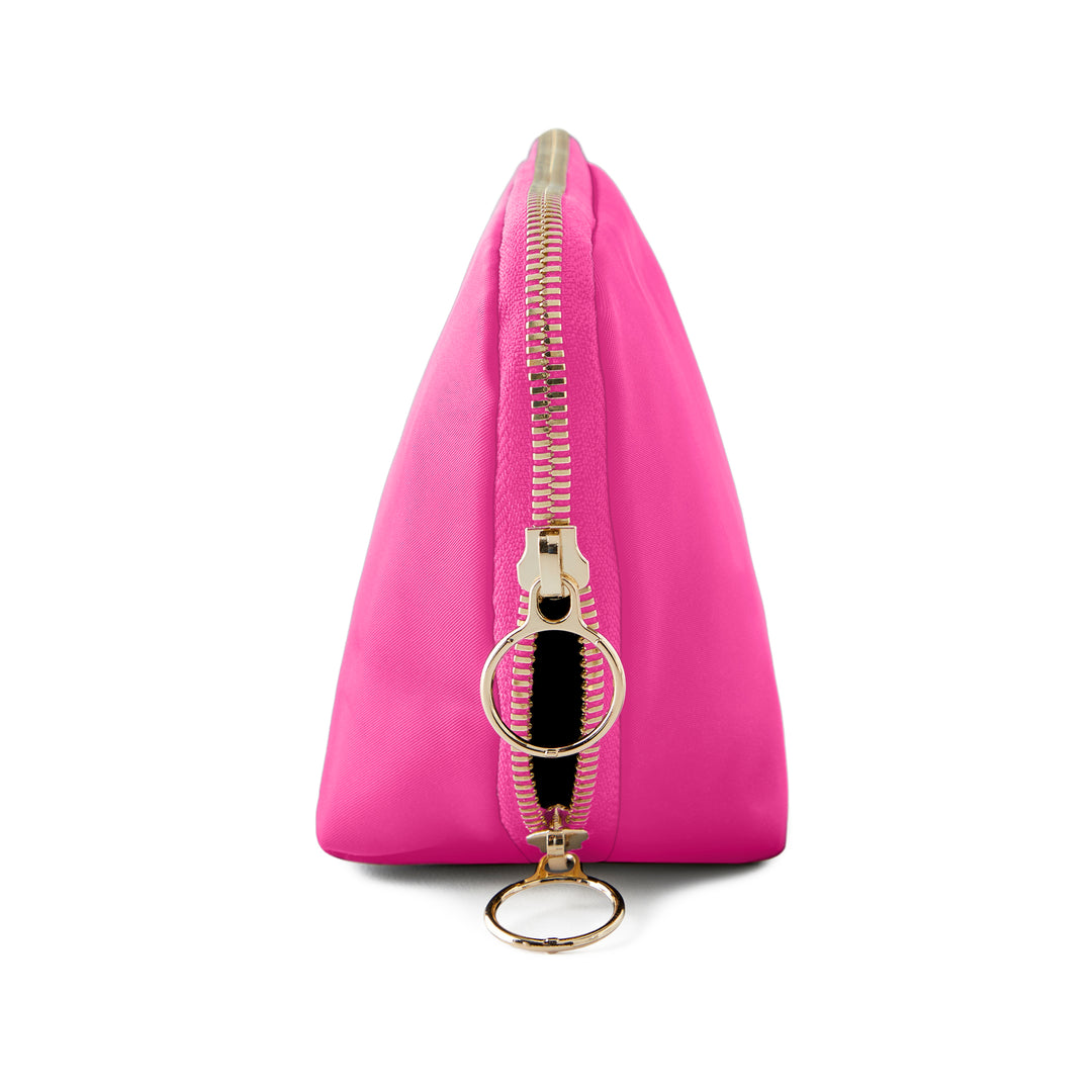 Studio photograph of a vibrant fuchsia triangular nylon cosmetic pouch on a white background featuring a polished gold-tone zipper and two oversized circular ring pull tabs