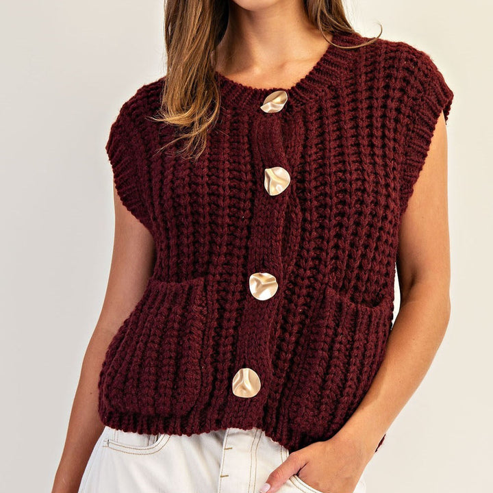 Close-up of a burgundy chunky knit vest with sculptural gold buttons and front pockets
