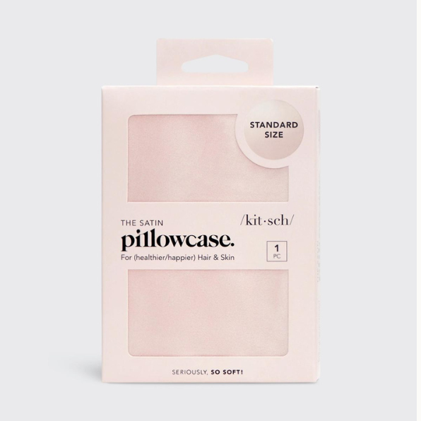Commercial product photography by Kitsch of a blush pink satin pillowcase in its retail box featuring rectangular window cutouts, a circular standard size seal, and elegant black branding