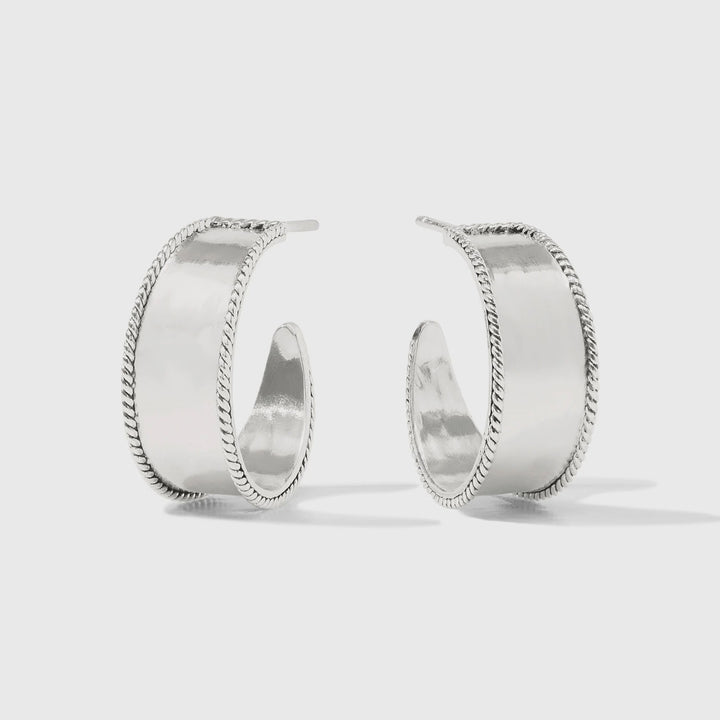 Sterling silver jewelry showcasing a pair of wide, open-back hoop earrings with high-polished central bands and intricate braided rope edges on a minimalist gray background