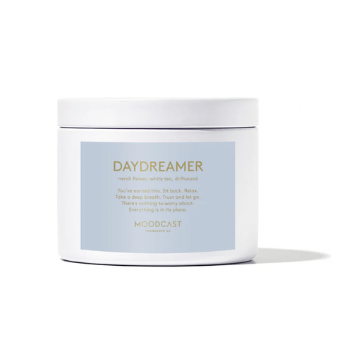 Studio photograph of a Moodcast Fragrance Co. Daydreamer candle featuring a white ceramic jar with a light blue label and gold metallic lettering listing notes of neroli flower and white tea against a white background