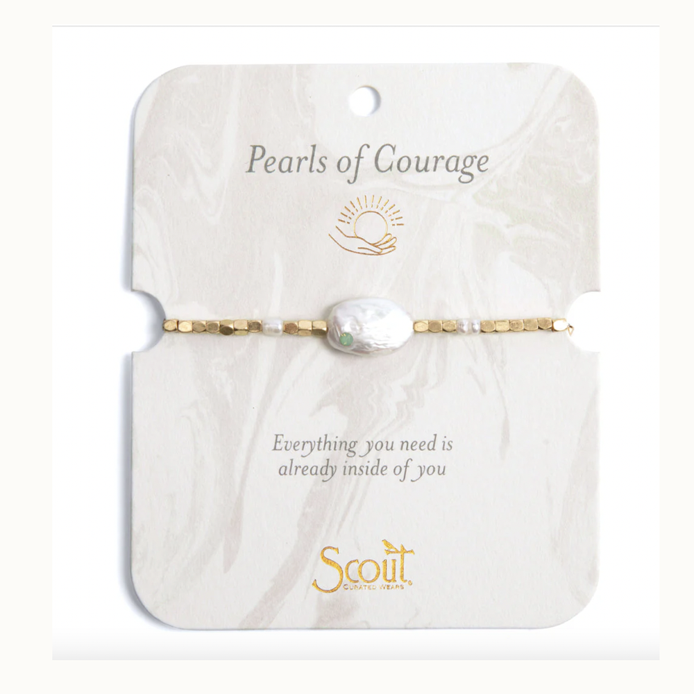 Jewelry by Scout Curated Wears featuring a Pearls of Courage bracelet on a marble-patterned card with a gold sun icon, a large irregular baroque pearl with a tiny green gemstone, and faceted gold-tone beads