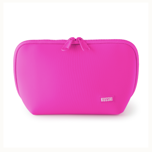 Studio product photograph of a Kusshi brand vibrant magenta makeup bag on a white background featuring a dual-pull zipper, rounded corners, and a small woven logo label