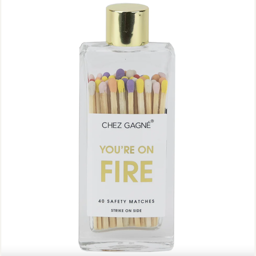 Product photograph by Chez Gagné of a clear glass bottle containing 40 safety matches with multicolored heads and a gold cap, featuring a white label with the text YOU'RE ON FIRE in yellow font against a plain white background