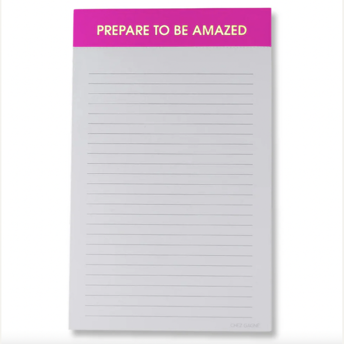 Stationery by Chez Gagné featuring a centered lined notepad with a vibrant hot pink header containing the gold-lettered phrase PREPARE TO BE AMAZED and thin gray horizontal lines on a light background