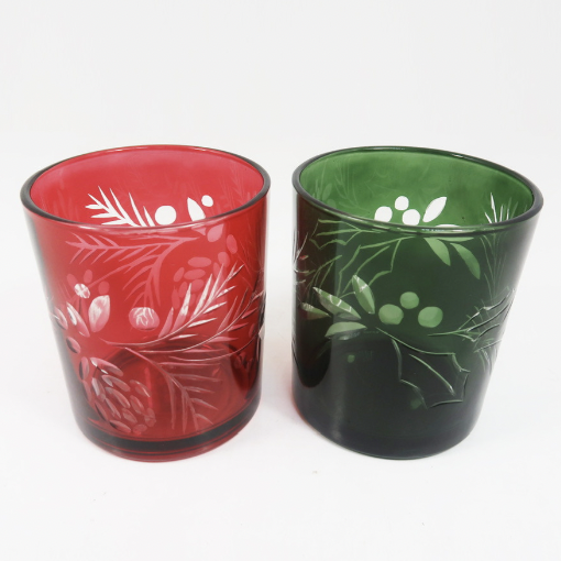 Two etched glass tumblers, one red with pine and pinecones and one green with holly