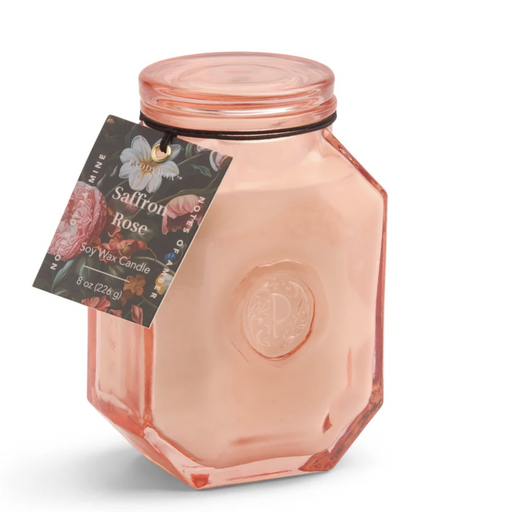 Product photograph by Paddywax of a Saffron Rose soy wax candle in a peach-toned hexagonal glass jar featuring an embossed seal and a dark floral hangtag with colorful botanical illustrations on a white background
