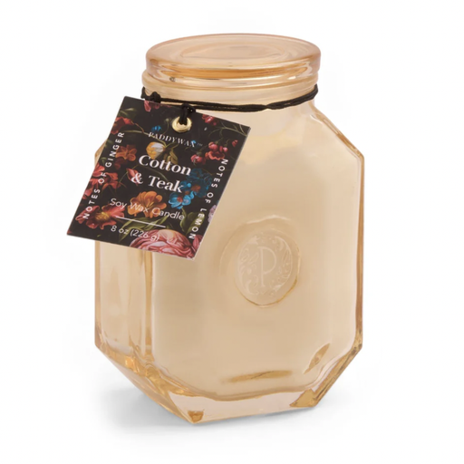 Paddywax Cotton and Teak soy wax candle in a peach-hued hexagonal glass jar featuring an embossed P logo and a decorative floral hangtag tied with a black cord