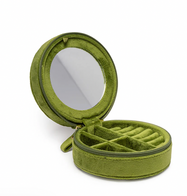 Studio photograph of a plush moss green velvet circular jewelry travel case featuring a built-in round mirror, multiple soft ring rolls, and divided internal compartments against a white background
