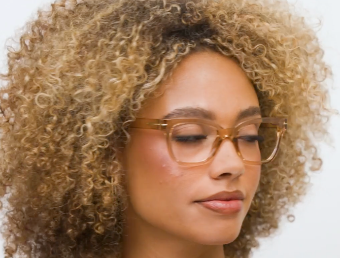 Woman with curly blonde hair looking down wearing translucent tan square glasses