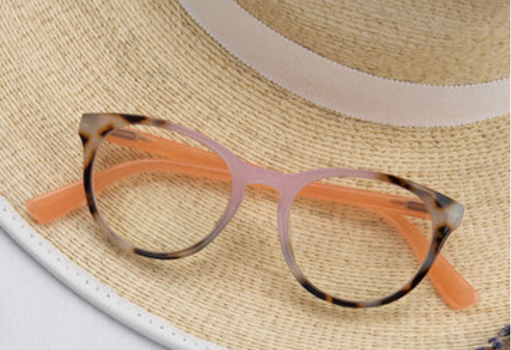 Tortoise and pink round glasses with peach temples resting on a straw hat