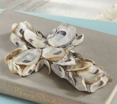 Handcrafted oyster shell sculpture of a decorative cross resting on a vintage cloth-bound book featuring iridescent pearly white interiors with dark purple muscle scars and rough tan outer edges