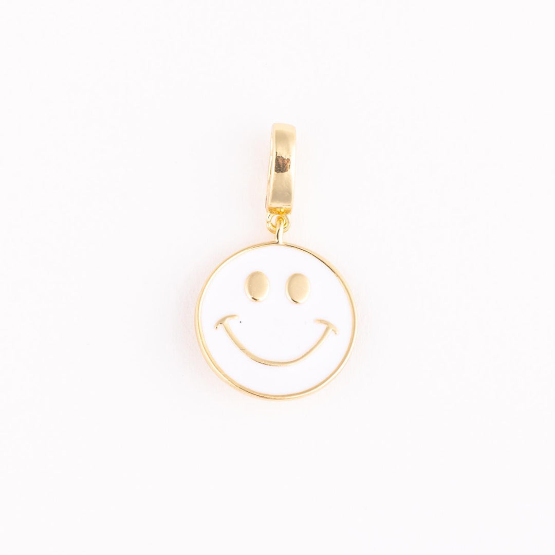 Gold and enamel jewelry charm of an iconic white smiley face centered on a plain background with polished gold trim, oval-shaped eyes, and a thin upturned smile
