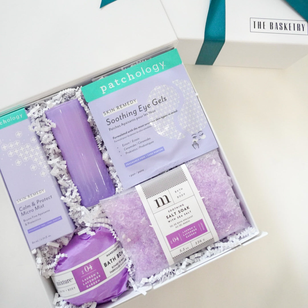 Photograph by The Basketry of a white spa gift box featuring Patchology Soothing Eye Gels and lavender bath products nestled in white crinkle paper with a decorative teal ribbon accent