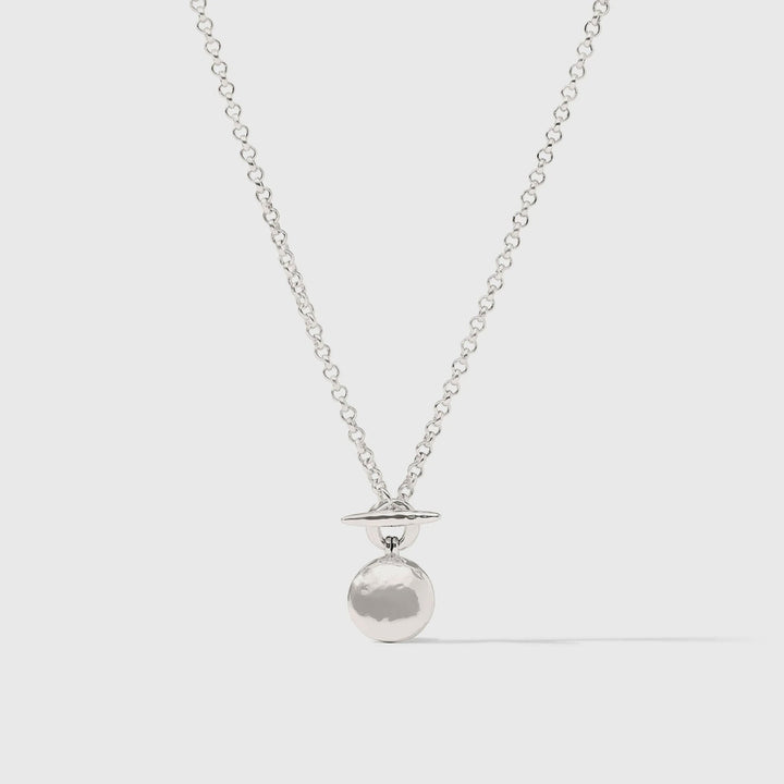 Silver-toned brass necklace by Celine featuring a Saturn-inspired pendant with a hammered-texture orb and thin horizontal ring suspended from a reflective link chain against a plain light grey background