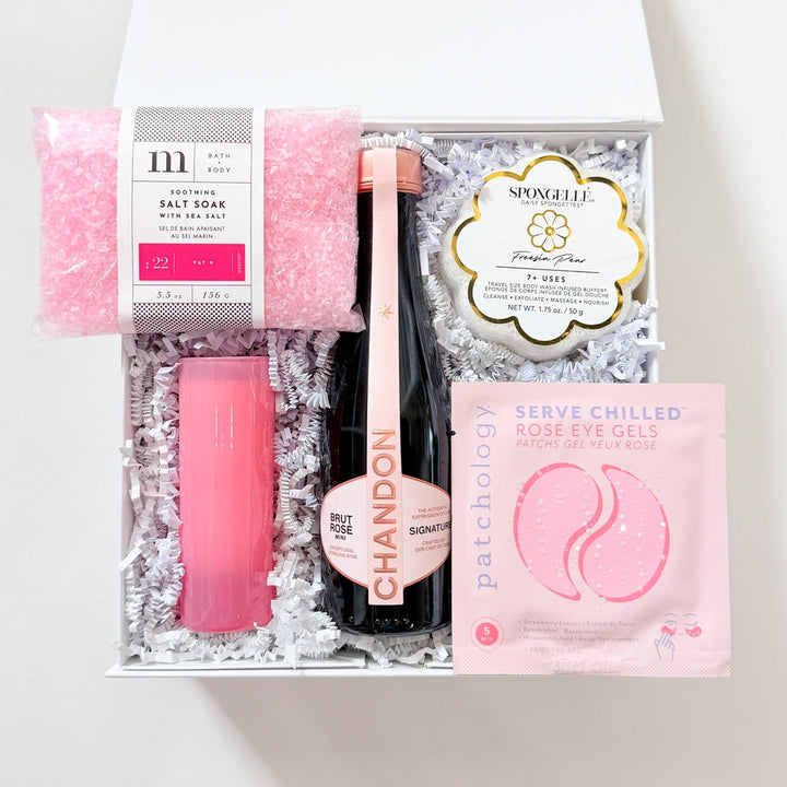 Set of beauty products including a pink lip balm, black nail file, and other items in a clear box on a white background.