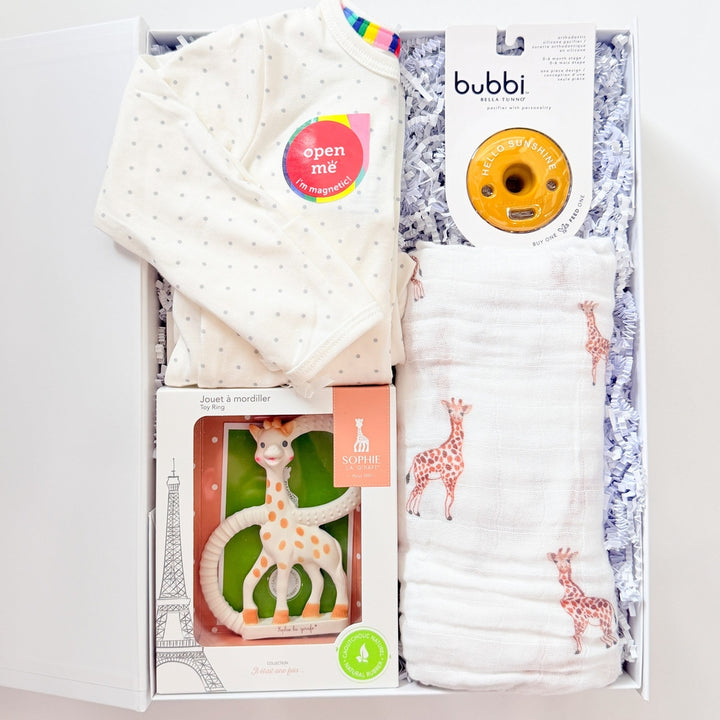 Baby gift set with white hat, diapers, and other items in a box on a light gray background