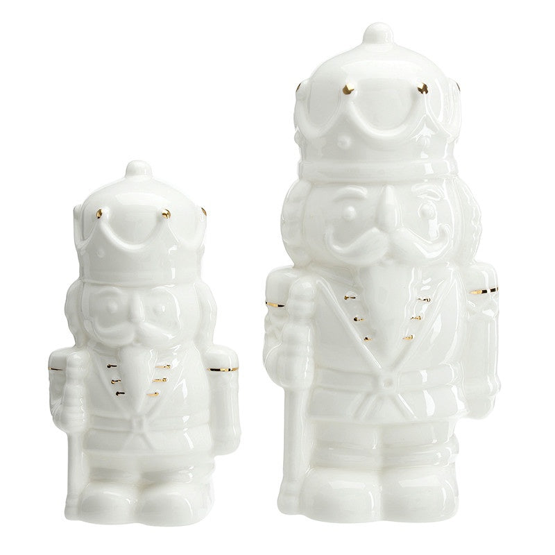 White glazed ceramic nutcracker figurines of varying heights standing on a plain white background featuring traditional holiday soldier forms with sculpted moustaches and delicate gold-painted accents on their uniforms and crowns