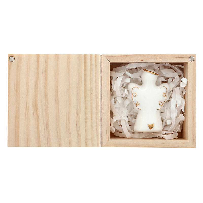 Porcelain figurine of a small white angel nestled in shredded paper inside an open light-toned wooden box featuring delicate gold-painted accents on the halo, wings, and a tiny heart at the base