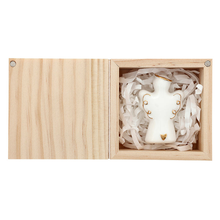 Porcelain figurine of a small white angel nestled in shredded paper inside an open light-toned wooden box featuring delicate gold-painted accents on the halo, wings, and a tiny heart at the base