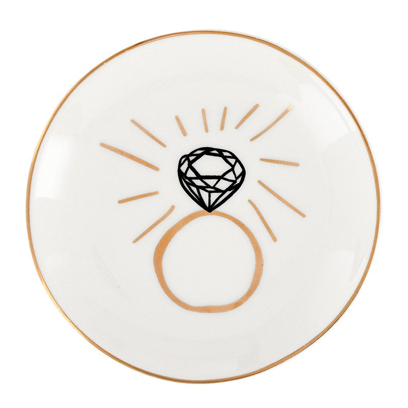 Ceramic trinket dish featuring a central diamond ring graphic with a metallic gold rim, radiating gold accent lines, and a black-inked faceted gem icon