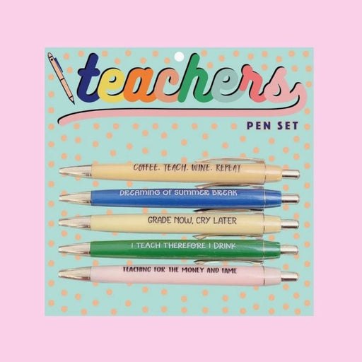 Product photography of a Teachers Pen Set featuring five retractable ballpoint pens with vibrant barrels in yellow, blue, cream, green, and pink displayed on a mint green polka-dotted backing card with humorous engraved slogans including Grade Now, Cry Later and Dreaming of Summer Break under a multi-colored cursive heading