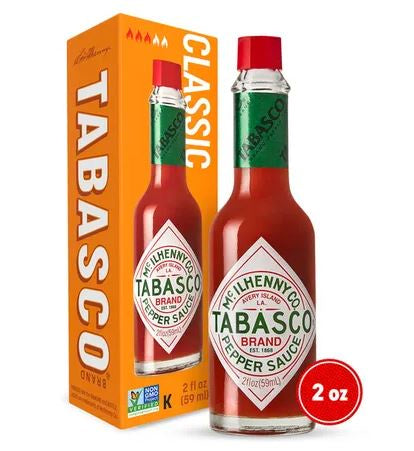 Commercial product photograph by McIlhenny Company of a 2 oz bottle of Tabasco Brand Pepper Sauce and its orange box on a white background, featuring the iconic diamond-shaped white label, a bright red screw cap, and green neck wrap